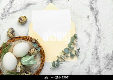 Envelope with blank greeting card, Easter eggs, bunny and eucalyptus branches on white marble background Stock Photo