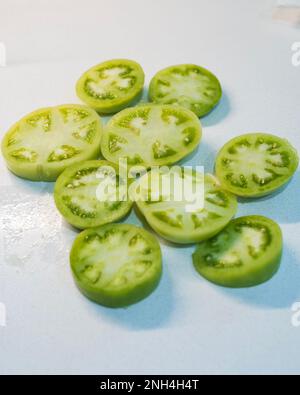 Sliced green tomatoes ready for breading and frying on a white background . Stock Photo