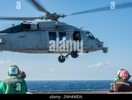 221213-N-UF592-1063 PHILIPPINE SEA (Dec. 13, 2022) Sailors observe as an MH-60S Sea Hawk, attached to the Golden Falcons of Helicopter Sea Combat Squadron (HSC) 12, takes off from the flight deck of the U.S. Navy’s only forward-deployed aircraft carrier, USS Ronald Reagan (CVN 76), in the Philippine Sea, Dec. 13. HSC 12, originally established as Helicopter Anti-Submarine Squadron (HS) 2 on March 7, 1952, is the oldest active operational Navy helicopter squadron. Ronald Reagan, the flagship of Carrier Strike Group 5, provides a combat-ready force that protects and defends the United States, an Stock Photo