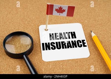 On the table is the flag of Canada, a pencil, a magnifying glass and a sheet of paper with the inscription - Health insurance Stock Photo