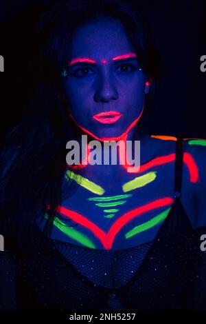 Fashion model woman in neon light, portrait of a beautiful model with fluorescent makeup, body art design in UV, painted face, colorful makeup, on a b Stock Photo