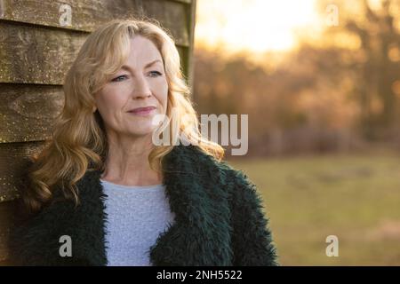 Attractive thoughtful middle aged woman smiling outside at sunset Stock Photo
