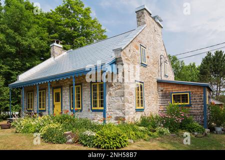 Old 1841 cottage style fieldstone house facade with Hosta plants, Hemerocallis flowers in border and cedar shingles extension in summer. Stock Photo