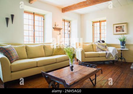 Beige upholstered sofas with mixed cushions and antique grain scale coffee table in living room inside old 1841 house. Stock Photo