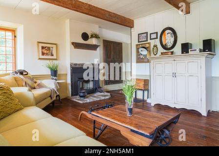 Beige sofas with mixed cushions, antique grain scale coffee table, white wooden television cabinet, wood burning fireplace in living room of old home. Stock Photo