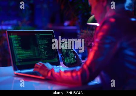 Seen from behind modern woman with laptop and smartphone protecting network against cyberattack from hackers on internet in modern office. Stock Photo