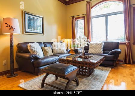 Brown leather sofas, ottoman and elaborately carved wooden glass top coffee table in upstairs den inside luxurious home. Stock Photo