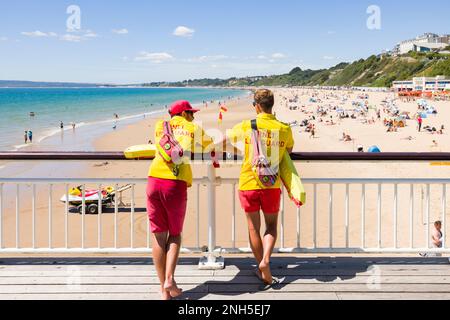 BOURNEMOUTH, UK - July 08, 2022. Two RNLI lifeguards in uniform watching Bournemouth beach from the pier during summer. Stock Photo