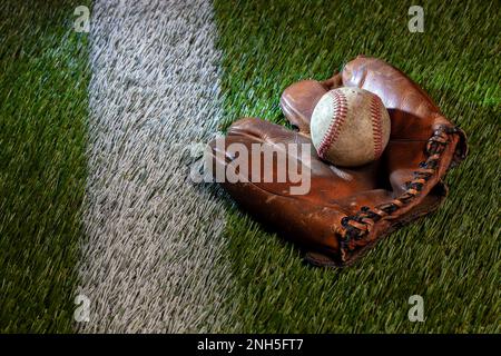 Old baseball in brown leather mitt on a grass field with white stripe Stock Photo