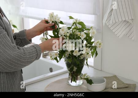 Woman making bouquet with beautiful jasmine flowers in kitchen, closeup Stock Photo