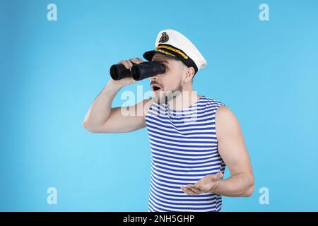 Sailor looking through binoculars on light blue background Stock Photo