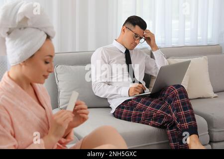 Man working on laptop while his wife relaxing in living room. Stay at home concept Stock Photo