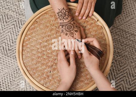 Master making henna tattoo on hand at table, top view. Traditional mehndi Stock Photo