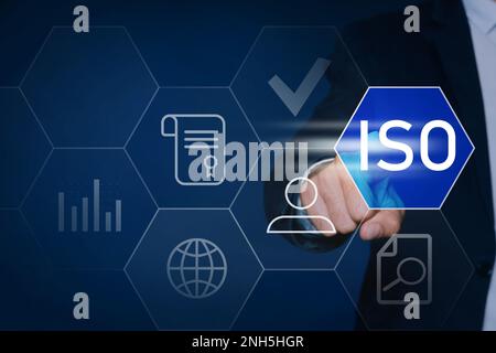 Businessman pointing at virtual icon with text ISO on dark background, closeup Stock Photo