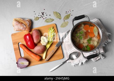 Pot of delicious vegetable bouillon and ingredients on light grey table, flat lay Stock Photo