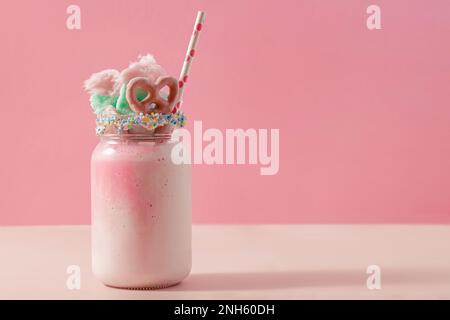 Delicious sweet strawberry milkshake in a glass jar, topped with a cotton candy and pretzel on pink background Stock Photo
