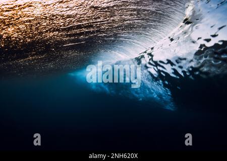Barrel wave breaking in ocean with sunset or sunrise light. Underwater view of surfing wave Stock Photo