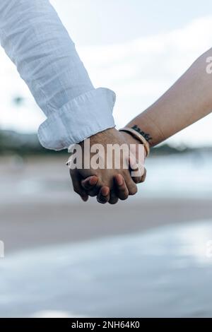 Couple holding hands while walking on the beach. Close up. Summertime Stock Photo