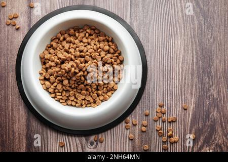 A bowl of dog food on a wooden floor. Dry food in granules. Stock Photo