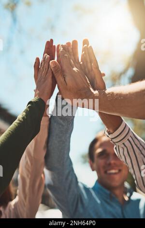 Put them up high guys. a group of cheerful young friends forming a huddle and giving each other a high five outside during the day. Stock Photo