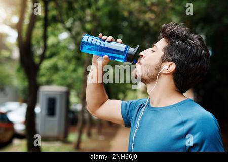 Nothing like water to refuel the engine. a sporty young man drinking water out of a bottle after having a jog outside during the day. Stock Photo