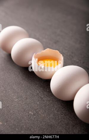 White chicken eggs and egg yolk in a row on black stone table. Very popular nutritious and economic food product. Concept image. Closeup view. Stock Photo