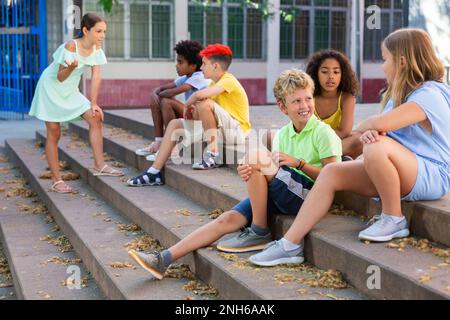 Happy tweenagers friends sitting on steps outdoors and chatting Stock Photo