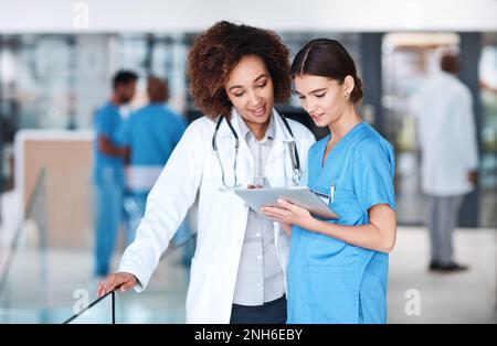 Medical collaborations in the age of the app. two medical practitioners using a digital tablet together in a hospital. Stock Photo