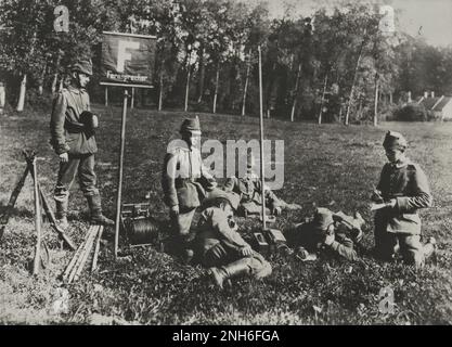1914-1918. World War I. Group of Austrian soldiers lying on a lawn where they have set up a mobile phone station. The sign 'Fernsprecher' refers to the presence of a telephone. One of the men lies on his stomach and talk on his headphones while he writes. On the left side you can see a cable drum and three rifles. Stock Photo