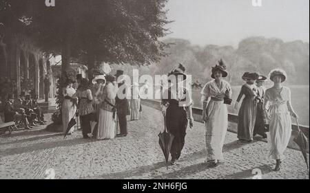 Paris seasons. Late afternoon at the Polo de Bagatelle. Paris, France. July 1913 It is on one of those sweet afternoons, when it is so pleasant to extend the time of the au Bois until the evening meal, conducive to light talks and elegant meetings... Among all the 'appointments' of good company, the Polo de Bagetelle, near Longchamp, offers itself as one of the most chosen. While, on the vast grass carpet reserved for the game, a rough race continues, among the gallopades and the blows of the mallet, peaceful groups wander along the fine sandy alley, or sit under the trees, opposing, in contra Stock Photo