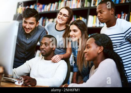 Study hard, study smart. a group of young students using a computer together in a college library. Stock Photo