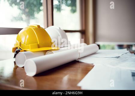 Yellow and white hard safety wear helmet hat placed on blueprint at construction site. Stock Photo