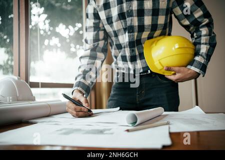 Close-up of asian male civil engineer working on blueprint architecture project on construction site at work desk in office. Stock Photo