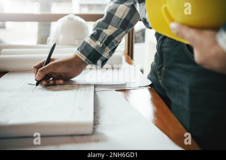Close-up of asian male civil engineer working on blueprint architecture project on construction site at work desk in office. Stock Photo