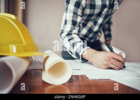 Close-up of asian male civil engineer working on blueprint architecture project on construction site at work desk in office. Stock Photo