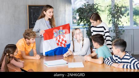 Smiling young woman teacher showing national flag of Croatia and telling preteens schoolchildren history of country during lesson in class Stock Photo