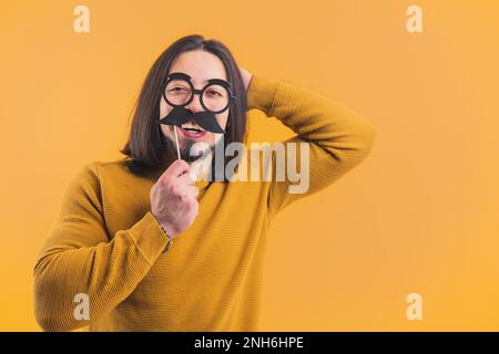 Joyful man holding moustache and glasses photo prop on a stick smiling at camera. High quality photo Stock Photo