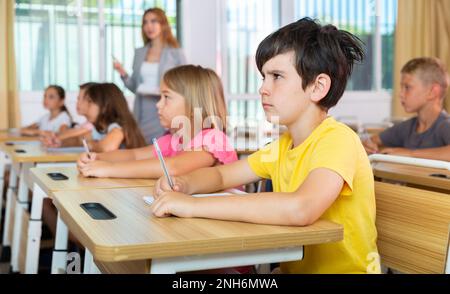 Tween boy listening to schoolteacher and writing in notebook in class Stock Photo