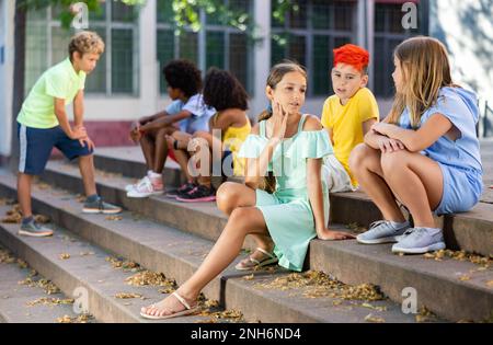 Positive tweenagers friendly blabbing while sitting on steps outdoors Stock Photo