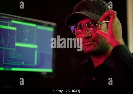 Portrait of cyber criminal adjusting glasses and looking at camera Stock Photo