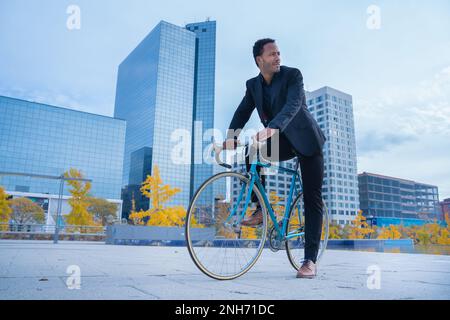 Stylish African American businessman in suit going to the office by bicycle in financial district.  Stock Photo