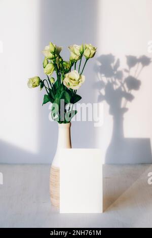 Bouquet of estouma flowers in vase and blank card on a table in sunlight. Mockup. Stock Photo