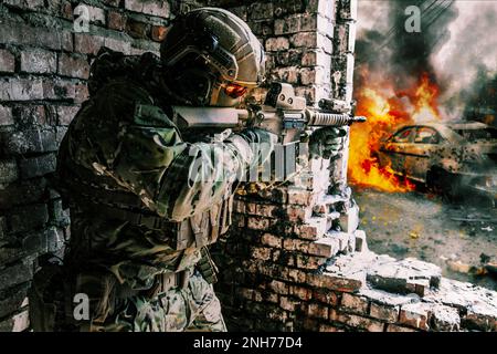 A soldier in action in a ruined building, danger of modern warfare. Fighting in destroyed building, engaged in combat with an unseen enemy. Armed with a firearm and other equipment. Concept of urban military war conflict Stock Photo