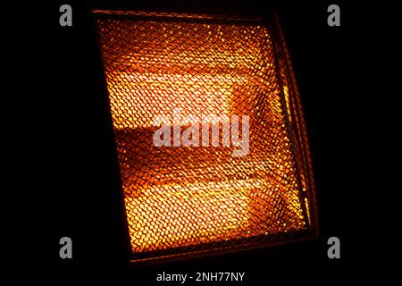 Glowing heating element of hot home electric heater. Orange warm light on black background Stock Photo