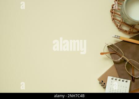 Brown notebook, calendar, eyeglasses, cup of milk, pencil on yellow desk background. flat lay, top view, copy space Stock Photo