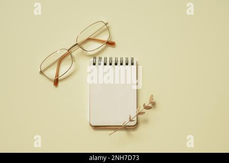 Blank notepad and eyeglasses on yellow desk background. flat lay, top view, copy space Stock Photo