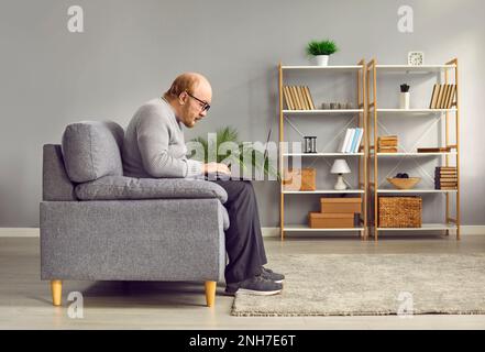 Side view portrait of elderly man sitting on sofa using laptop Stock Photo
