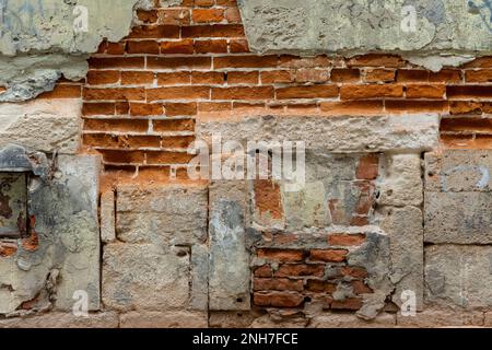 Grunge Background of Old Exterior Wall Built with Red Bricks and Sandstone Blocks with Peeling Plaster. Ruin and Decay Concept Stock Photo