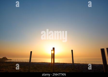 Amazing sunset on the beach, orange and blue colors, bright light coming through the posts Stock Photo