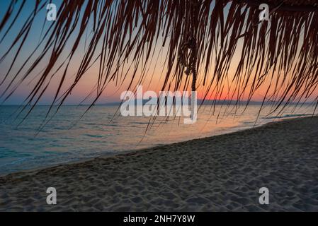 Straw umbrellas fluttering on Plaka beach at sunset, Naxos Stock Photo